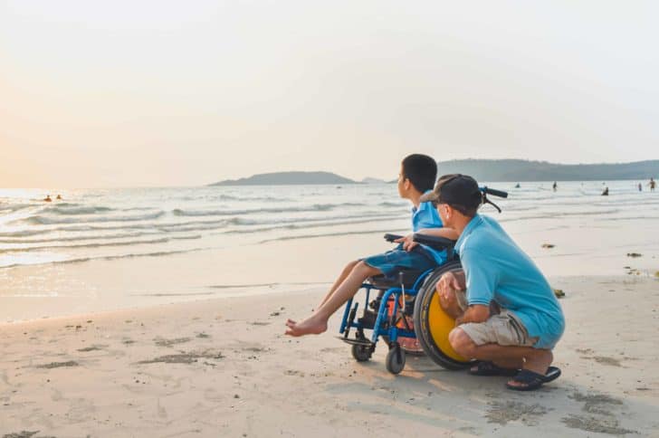 Man and child in wheelchair on beach.